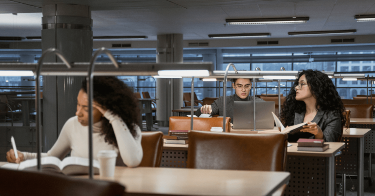 Δύο γυναίκες και ένας άντρας διαβάζουν για το μεταπτυχιακό τους στην βιβλιοθήκη ενός πανεπιστημίου